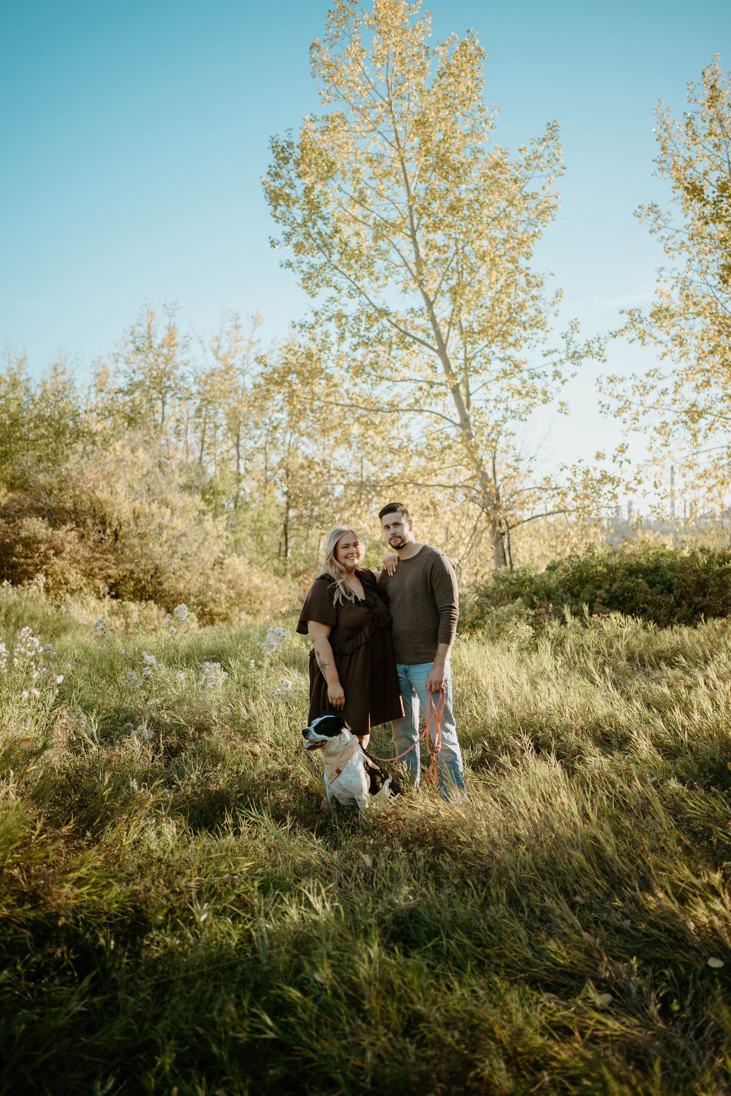 A couple walking together on a grassy hillside path among autumn trees on a sunny afternoon.