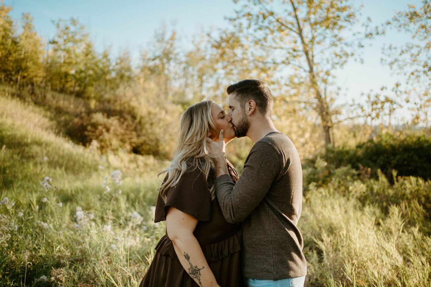 A couple shares a romantic moment in a sunlit meadow during golden hour.