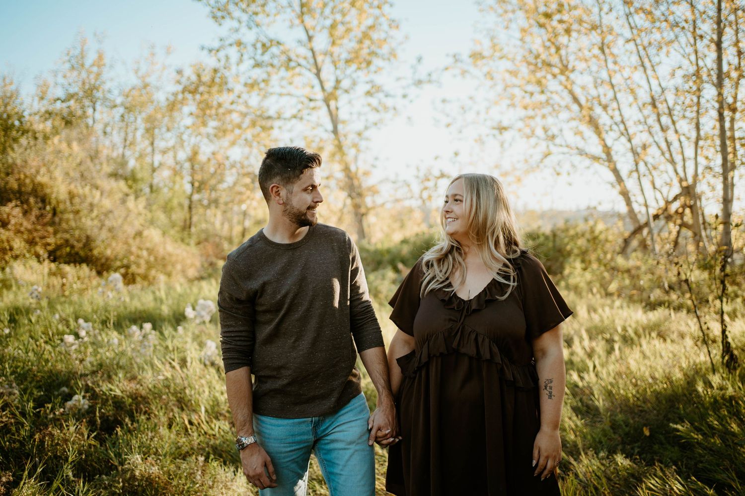 A couple shares tender moments together in a sunlit outdoor setting with autumn trees in the background.