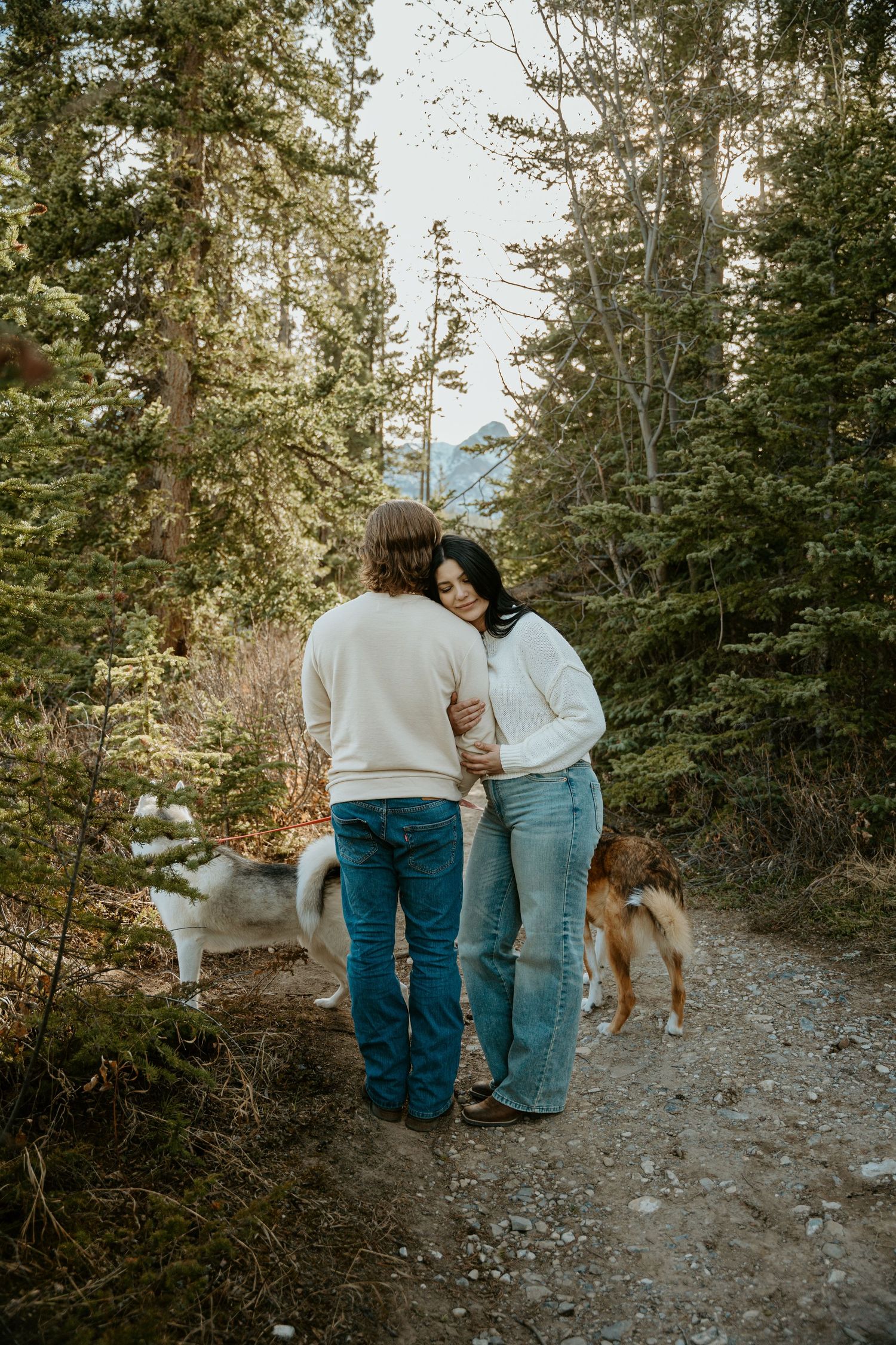 A couple walking on a mountain trail with their dog surrounded by evergreen trees on a misty afternoon.