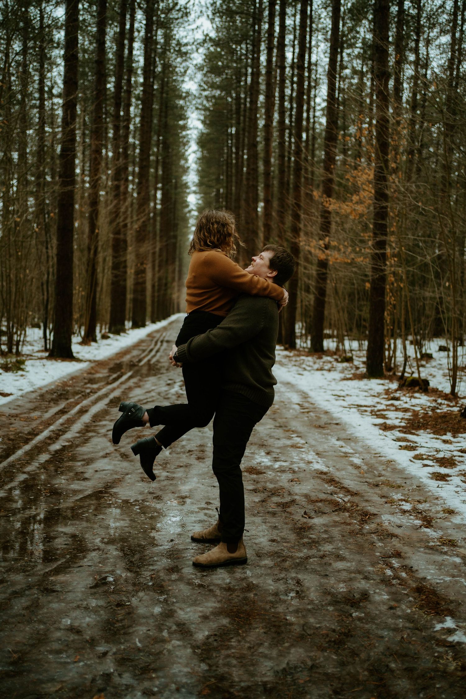A romantic winter moment as a couple spins on a snowy forest path.