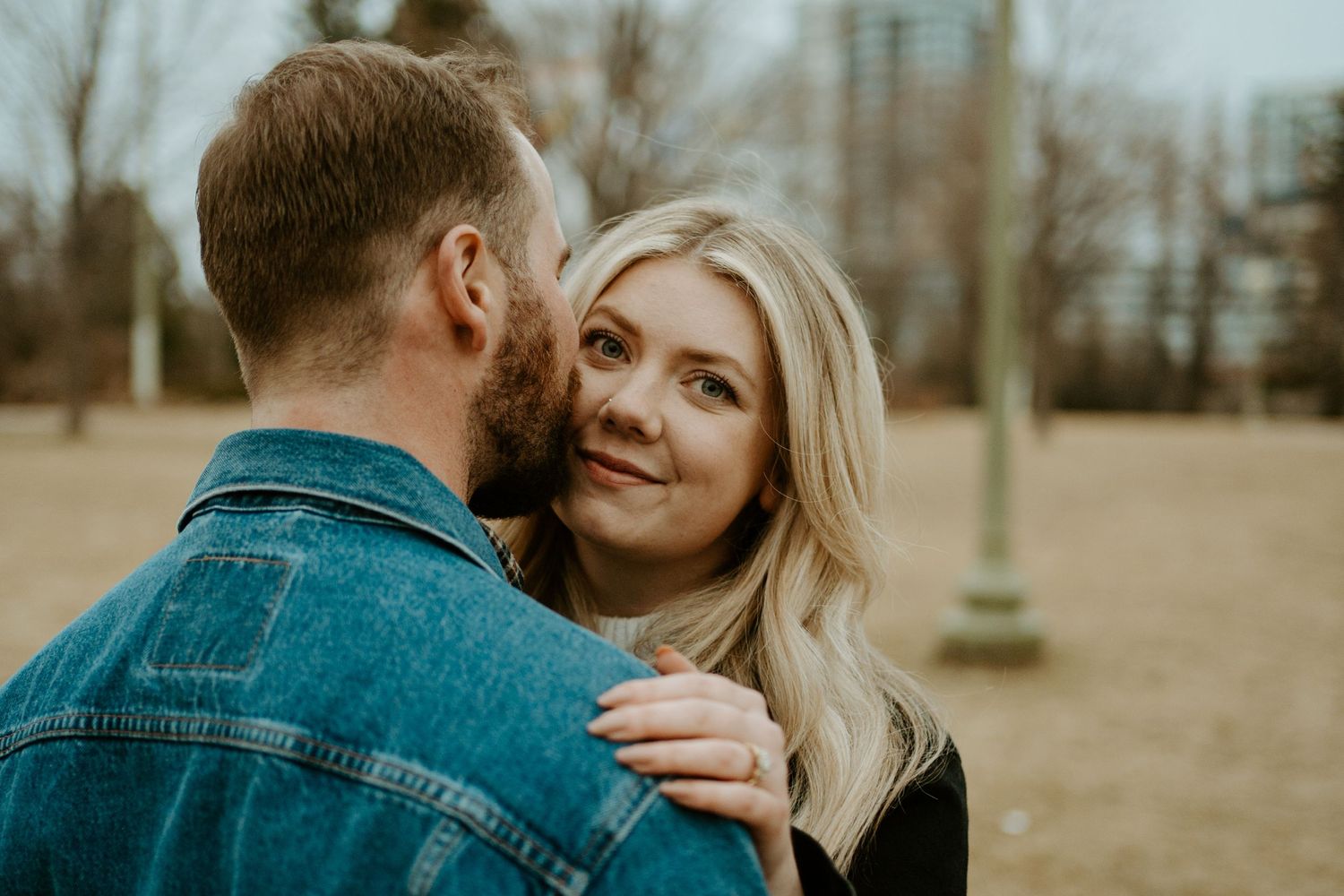 Tender moment between couple in denim jacket and black sweater during outdoor photoshoot.