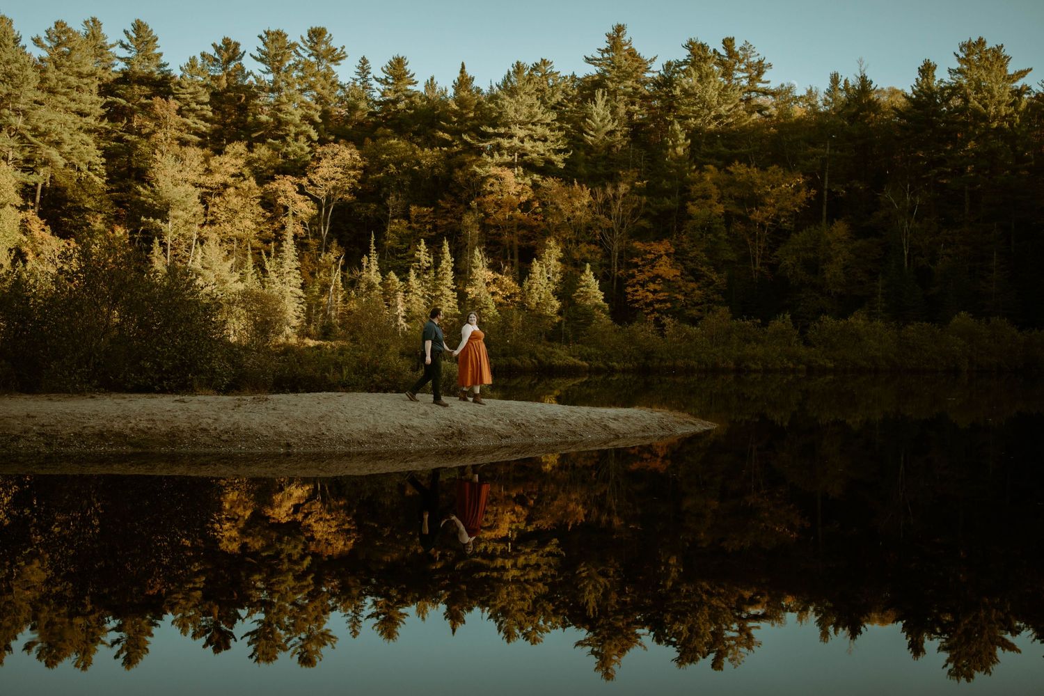 Tranquil lake surrounded by pine trees reflecting in still water during golden hour at sunset.