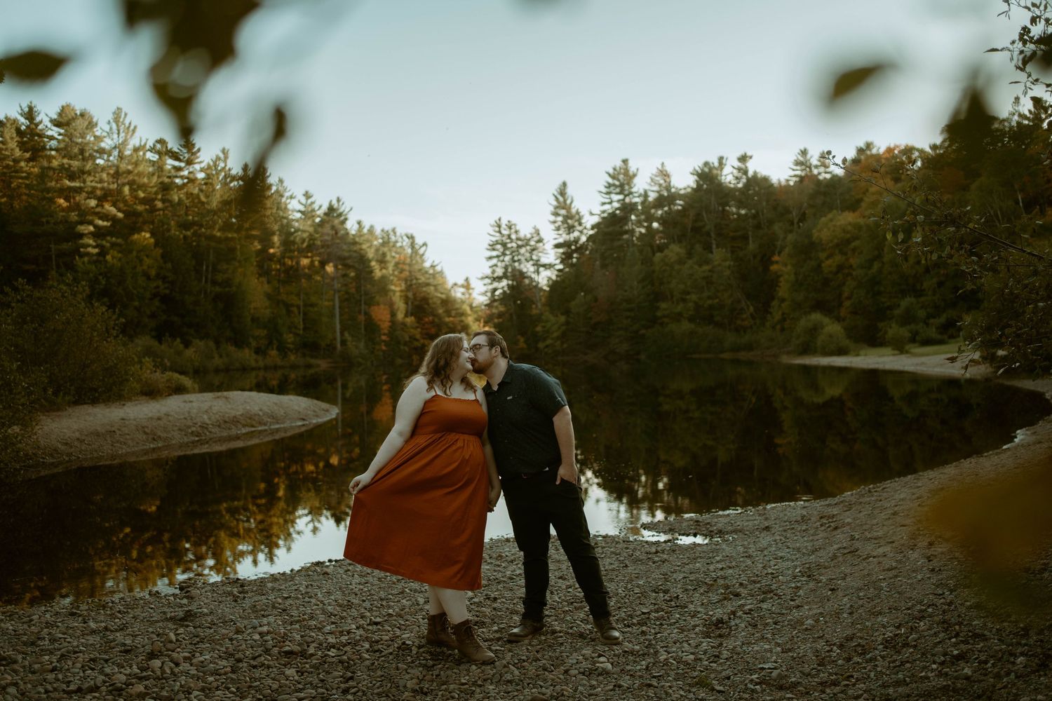 A romantic silhouette of a couple stands together against a misty forest lake backdrop during golden hour.