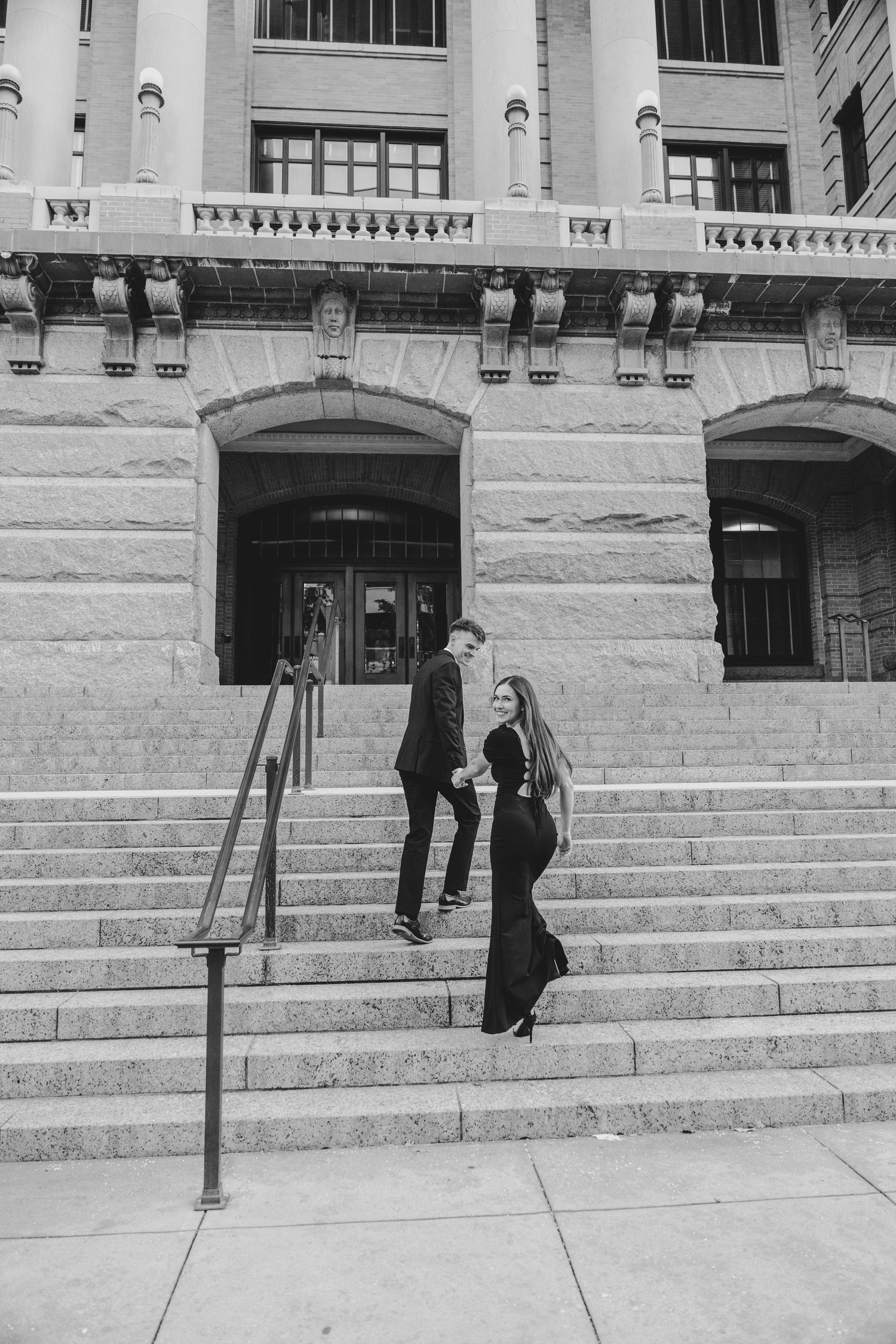 A couple stands together on grand stone steps of a historic building in black and white photography.