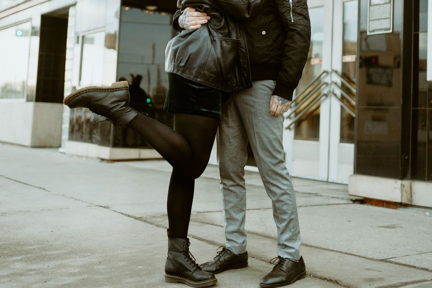 Two pairs of boots touching on a sidewalk in an artistic pose.