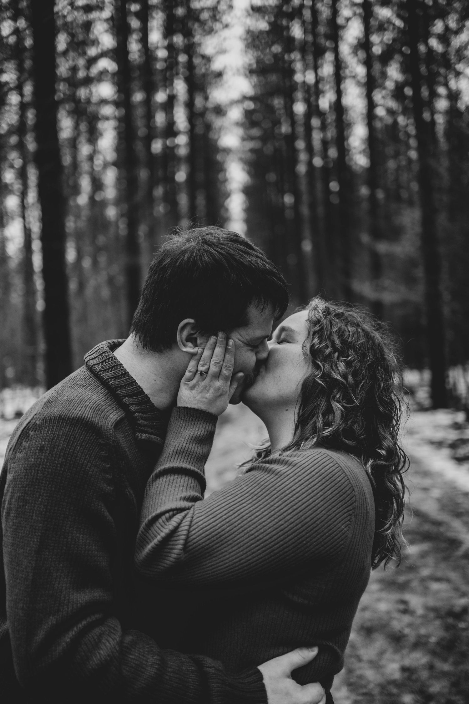An intimate black and white portrait of a couple sharing a tender moment in a winter forest.