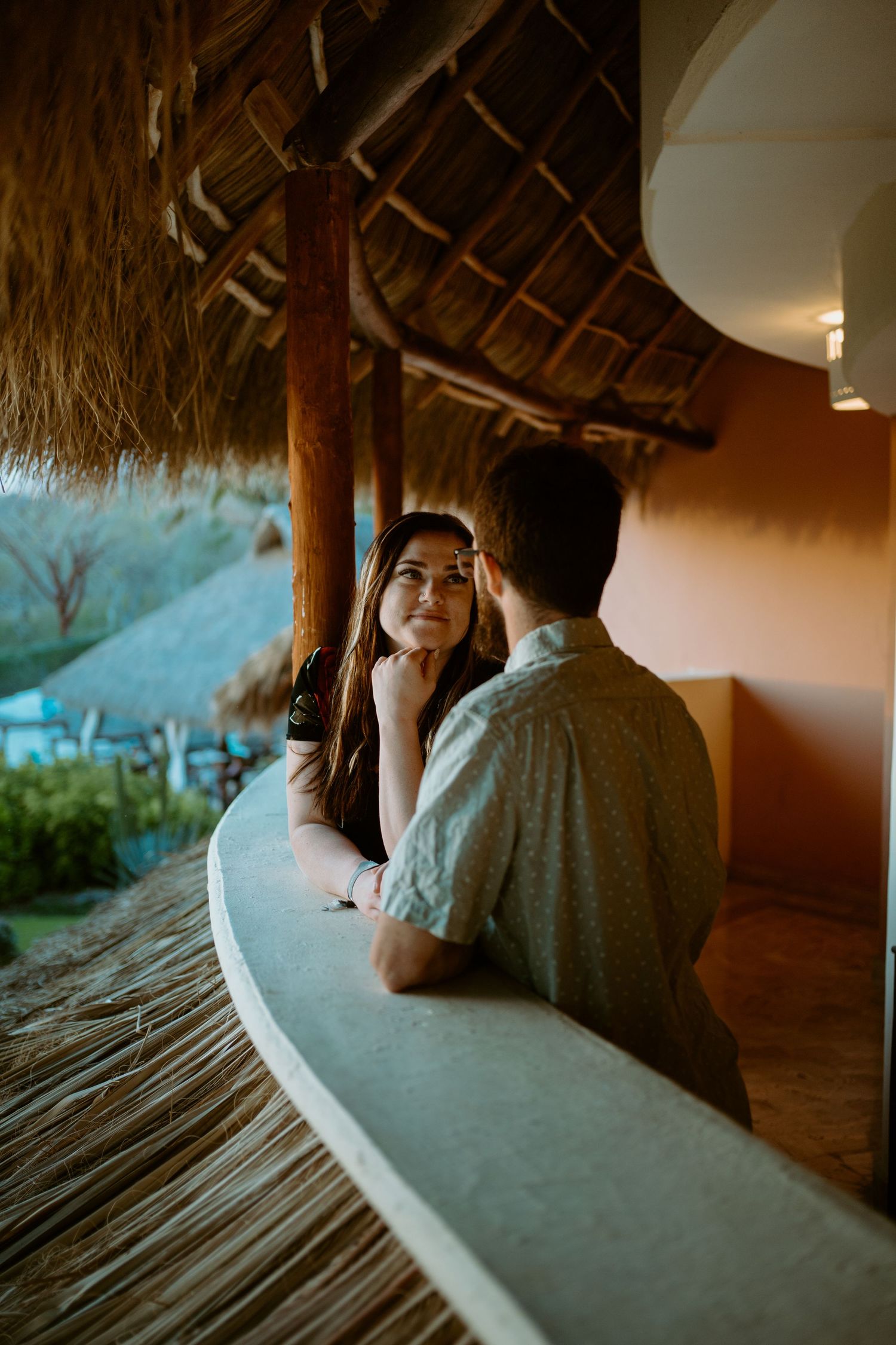 Romantic couple conversation at tropical thatched-roof bar during sunset.