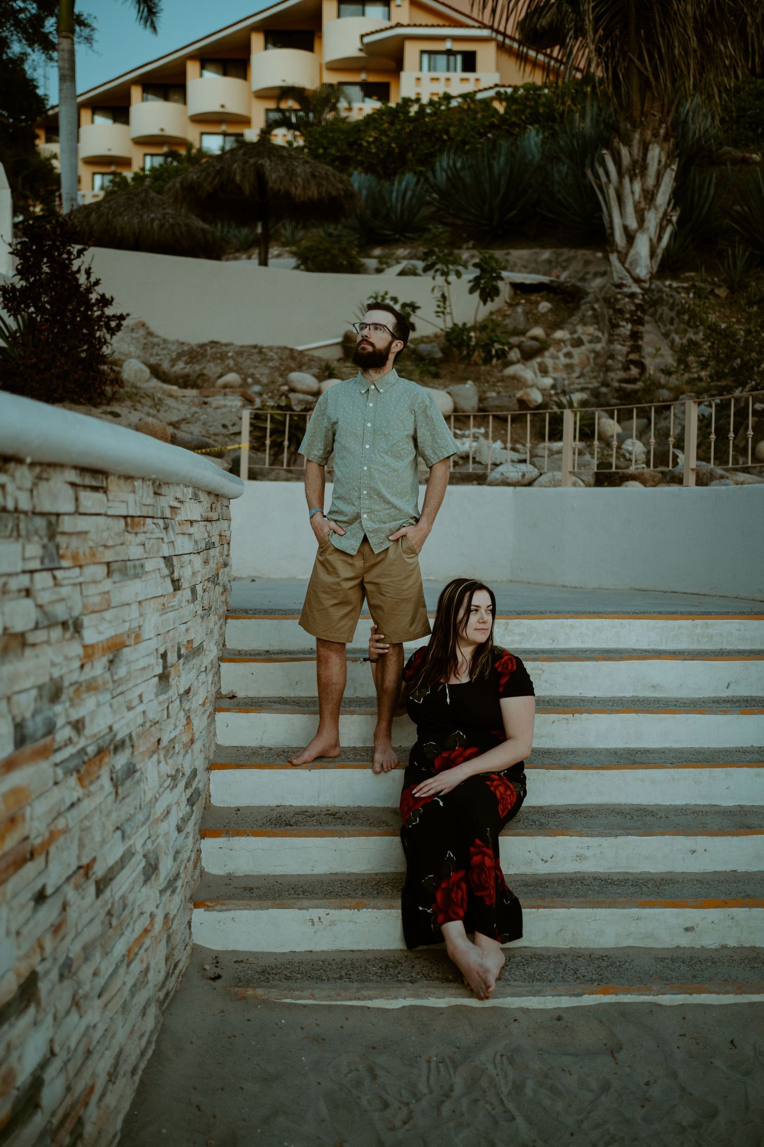 Stylish couple posing on stone steps of coastal resort during golden hour.