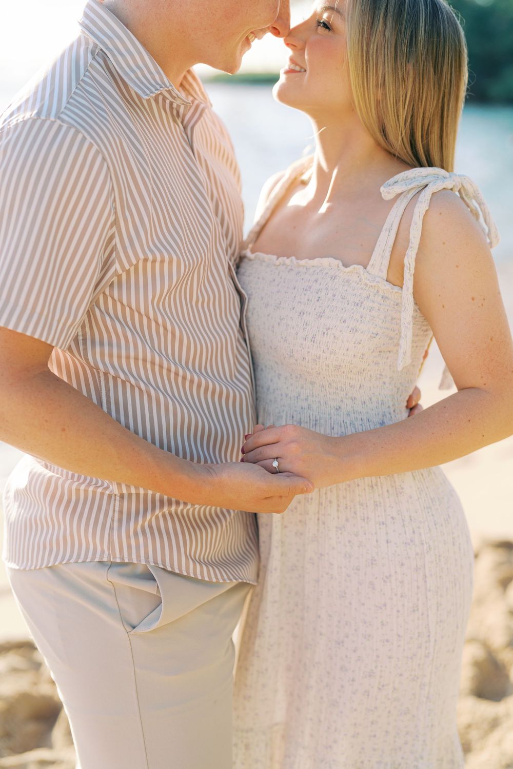 A couple in coordinating beige and white outfits embrace during a romantic outdoor photoshoot at sunset.