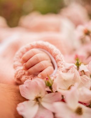Tiny newborn baby hand resting on delicate pink cherry blossoms with a soft pink knitted bracelet.