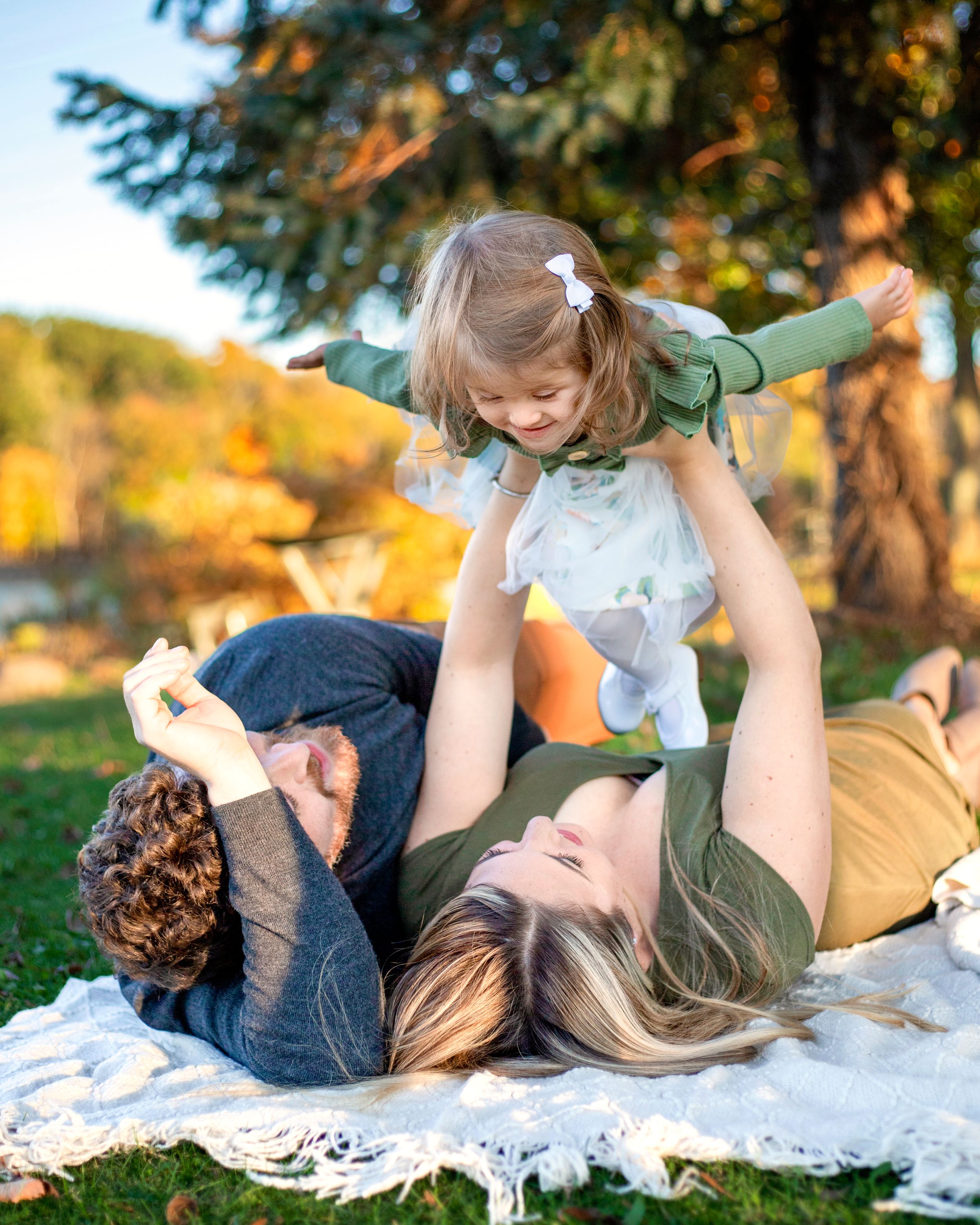 Best Bergen County Family Photographer captures family laying on blanket at Park in Mahwah, NJ.  Mom's flying girl in candid photo