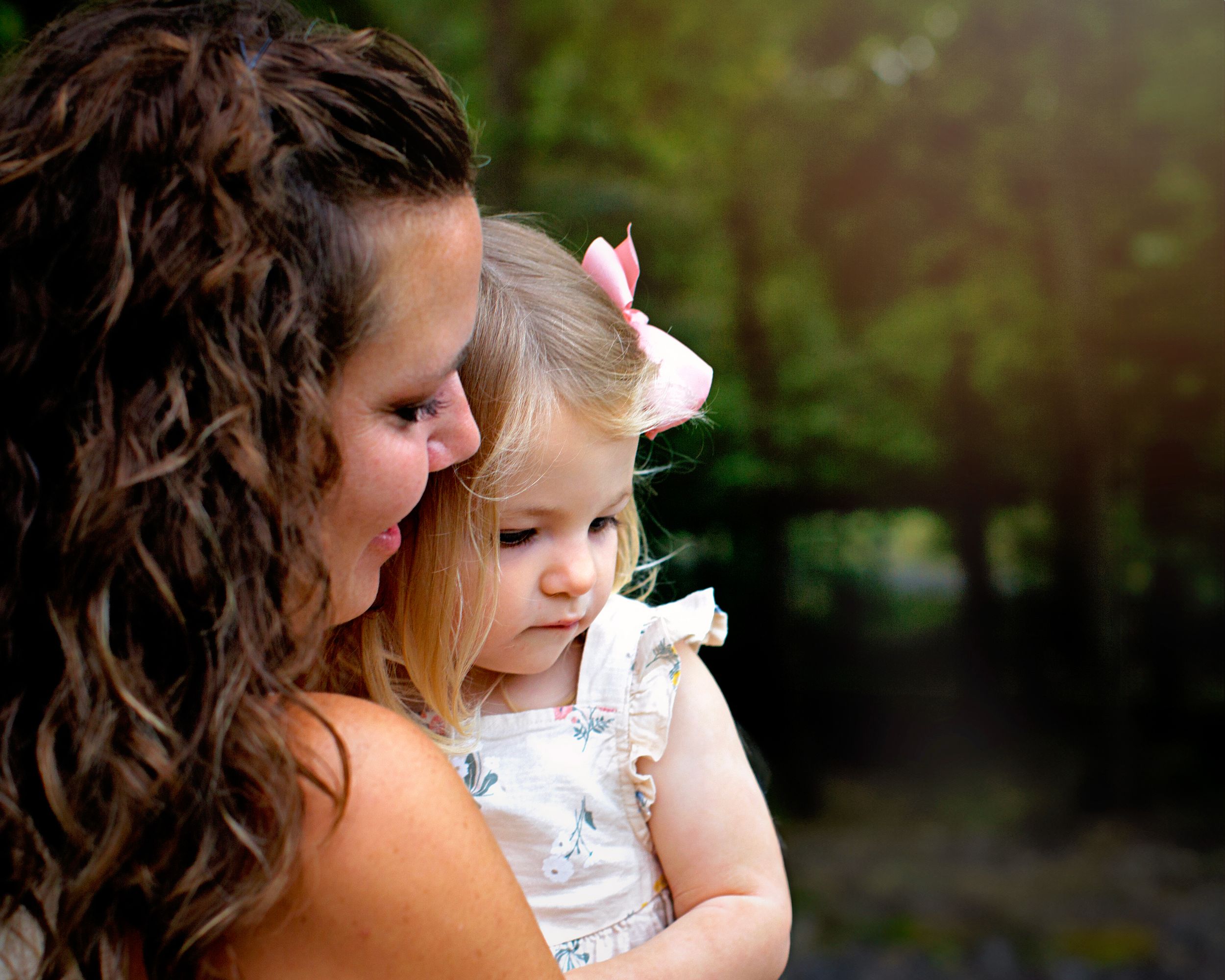 Mommy and me outdoor photography session near Ramsey, NJ.  Mother and daughter snuggling looking off to the side.  Girl wearing a pink bow.