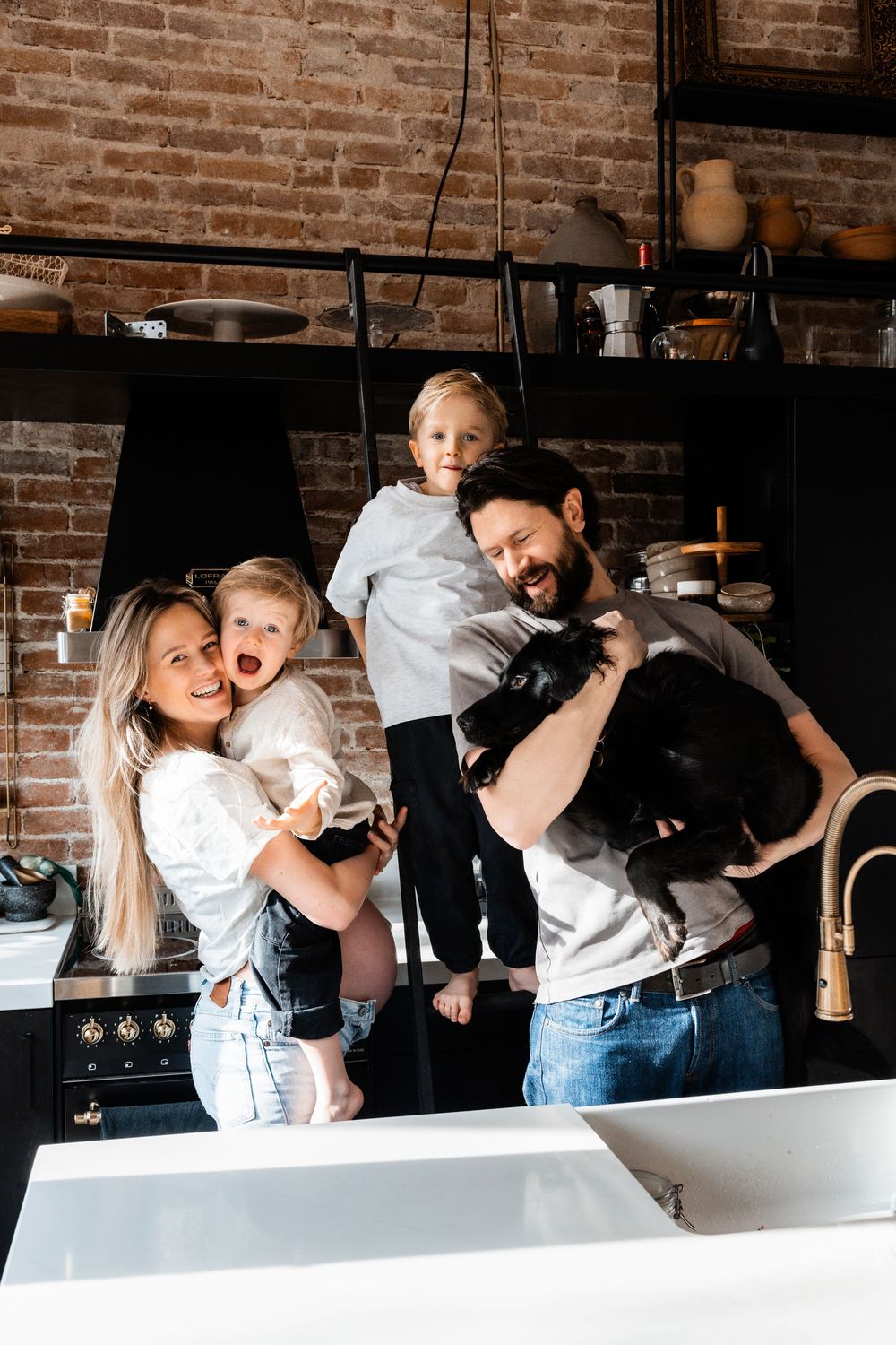 A joyful candid moment captured in a modern kitchen with exposed brick walls and dark appliances.