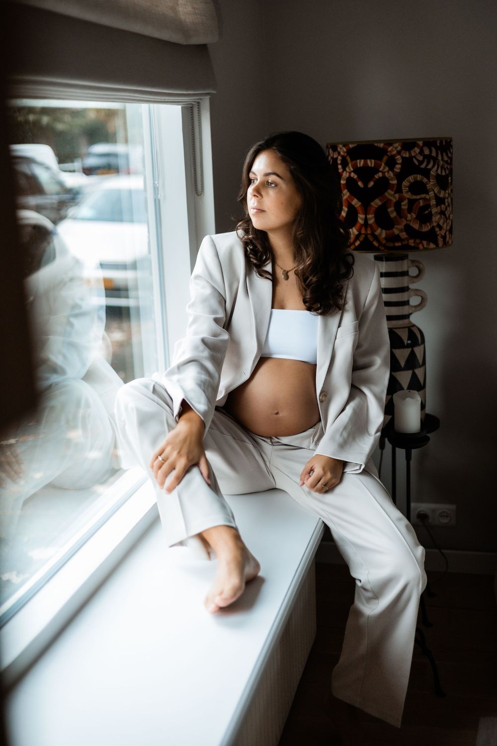 Zwangere vrouw bij het raam tijdens een lifestyle zwangerschapsfotoshoot