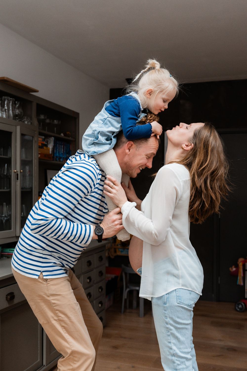 Playful family moment in kitchen as parent gives child shoulder ride while interacting with each other.