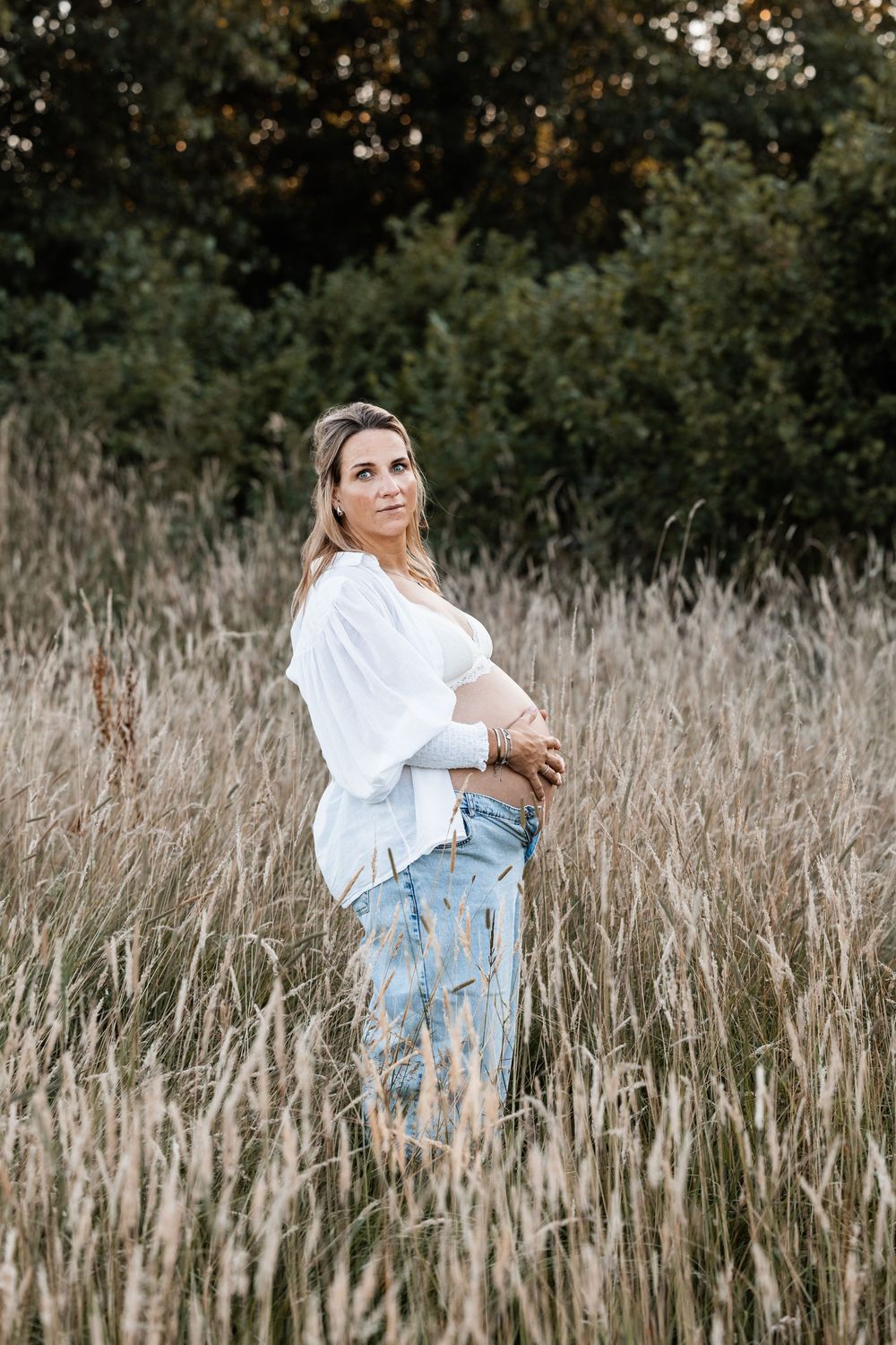 Zwangere vrouw in het hoge gras tijdens een zwangerschapsshoot in de natuur