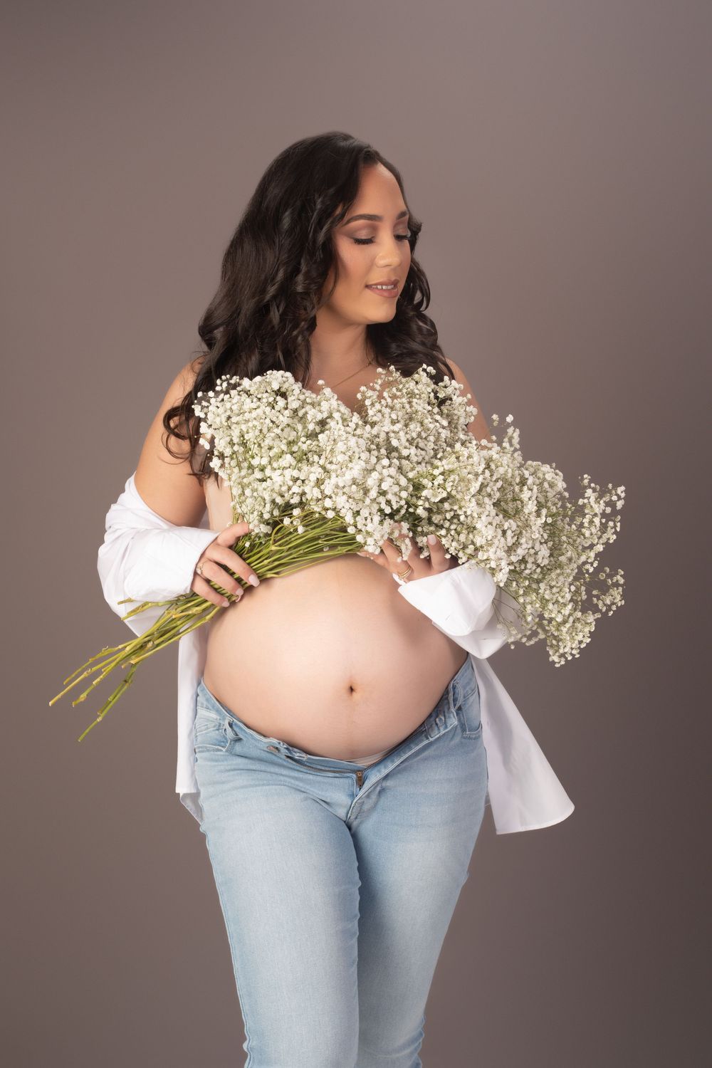 Maternity photos with white peasant top and baby's breath flowers against neutral backdrop.