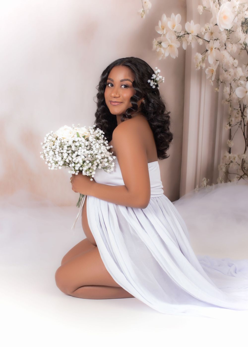 Maternity photoshoot featuring white fabric draping and delicate baby's breath flowers against a light backdrop.