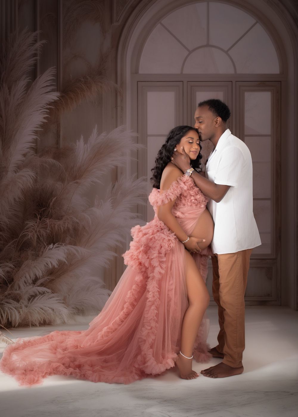 A romantic couple shares intimate moments in elegant poses while wearing pink tulle gown and brown suit in a studio setting.