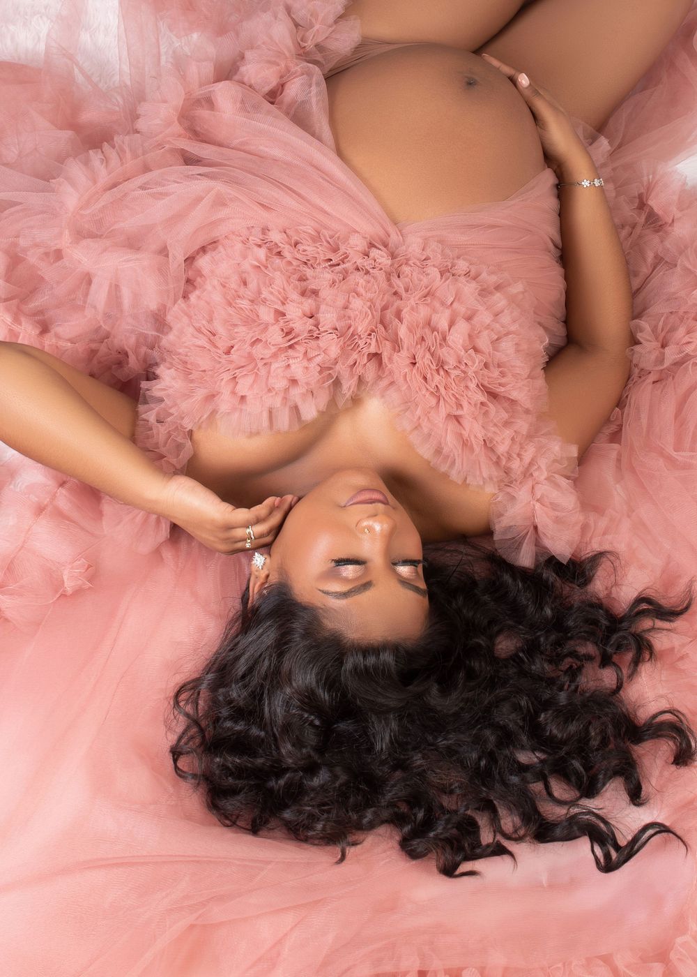 Someone reclines on pink tulle fabric wearing professional boudoir clothing in a series of artistic poses.