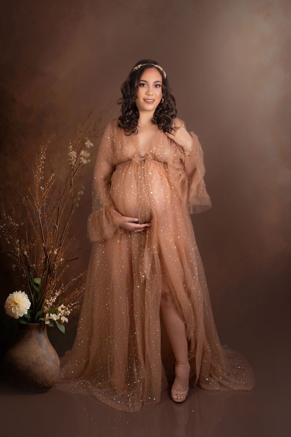 Elegant maternity portraits with flowing gold sequined dress and floral backdrop.