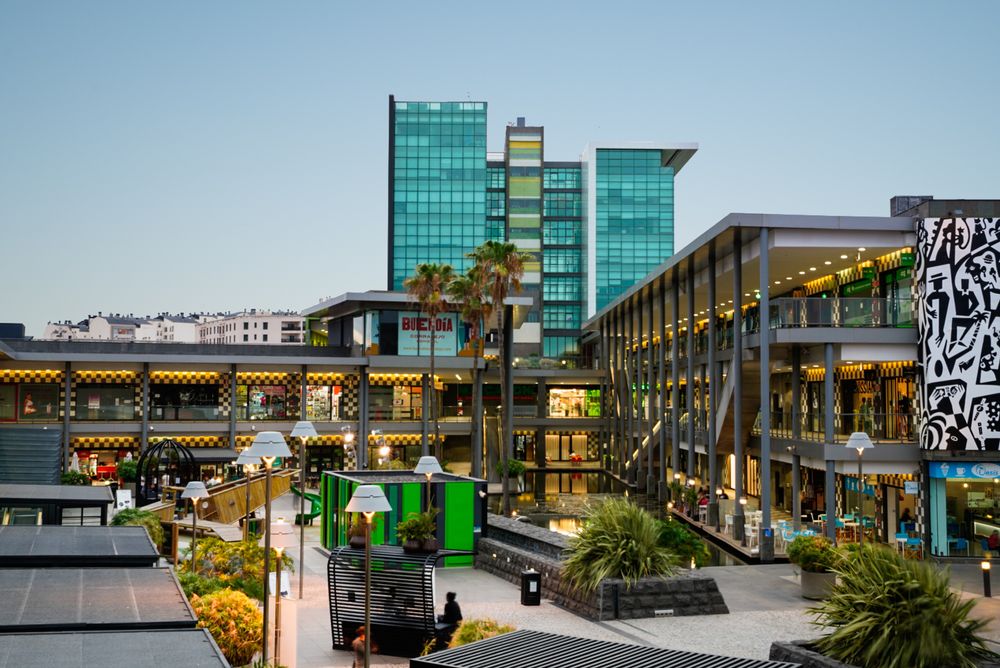 Modern glass office building with retail spaces and landscaped courtyard at dusk.