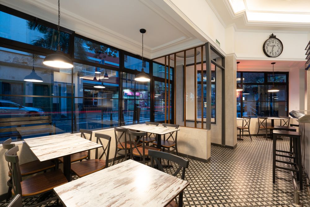 Restaurant interior with marble tables and geometric floor pattern illuminated by pendant lighting.