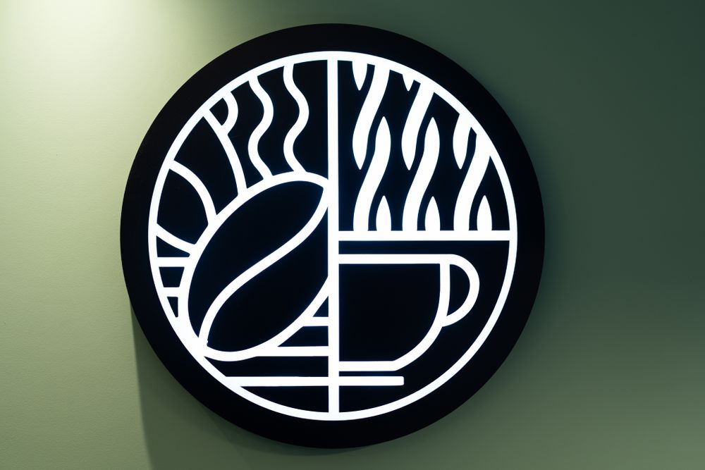 Close-up of minimalist black circular logo with coffee bean and cup design on green wall.