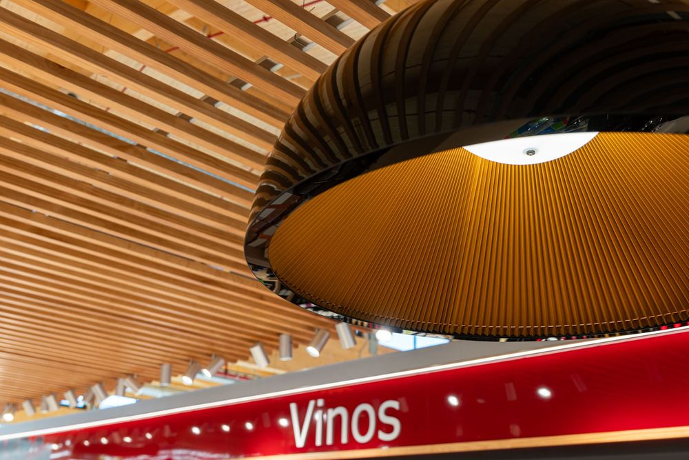 Large circular pendant light fixture above wine section with wooden slatted ceiling design.