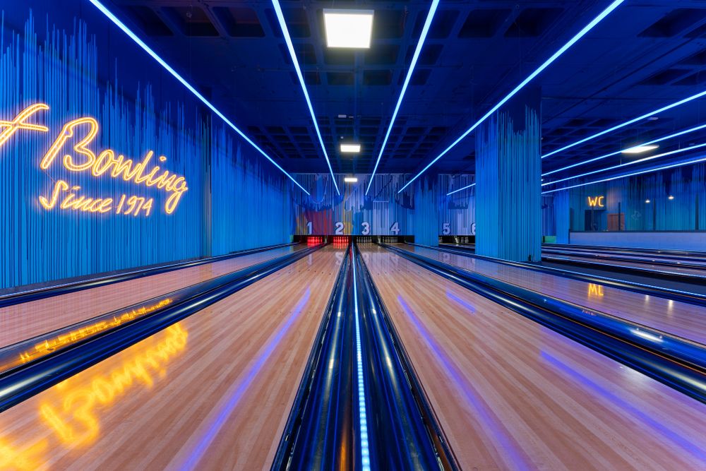 Bowling alley lanes with neon blue lighting and 'Home of Bowling' signage creating dramatic perspective.