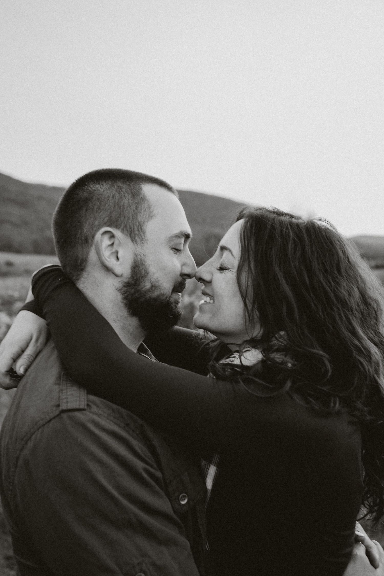 A romantic black and white photo of a couple embracing and sharing an intimate moment outdoors against a rural landscape in califon nj.