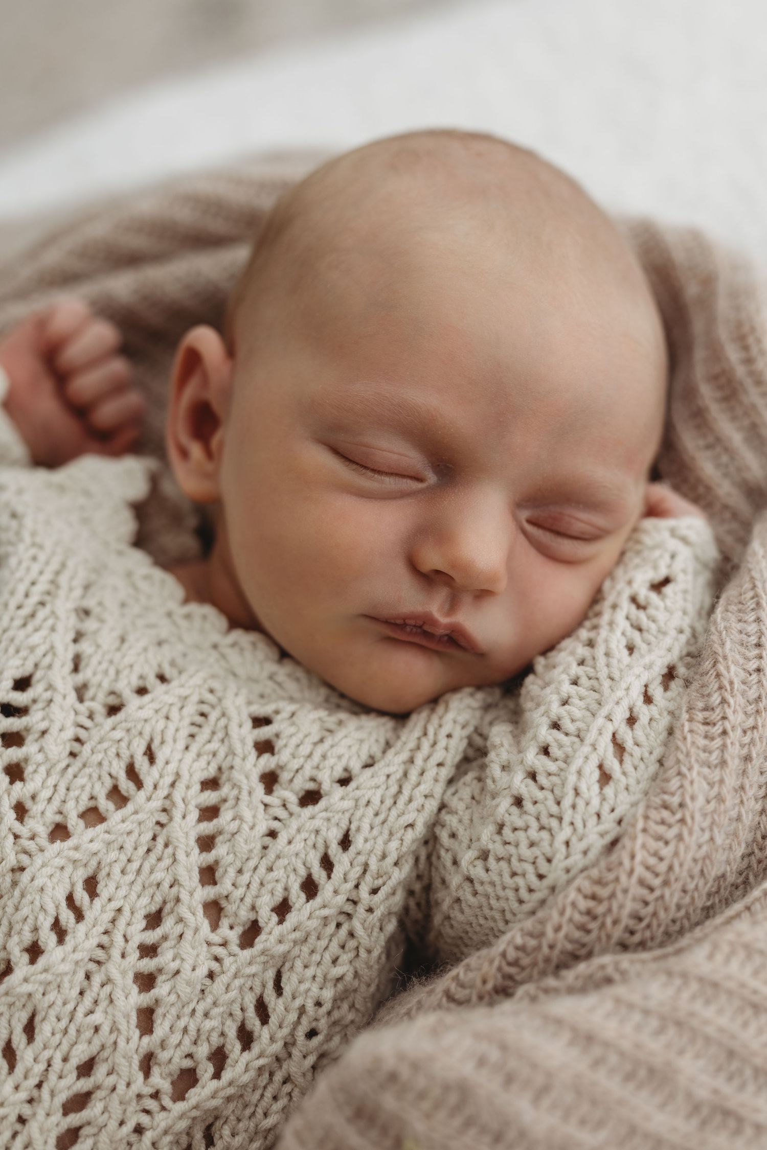 Newborn baby sleeping in a white wrap, photographed in natural light.