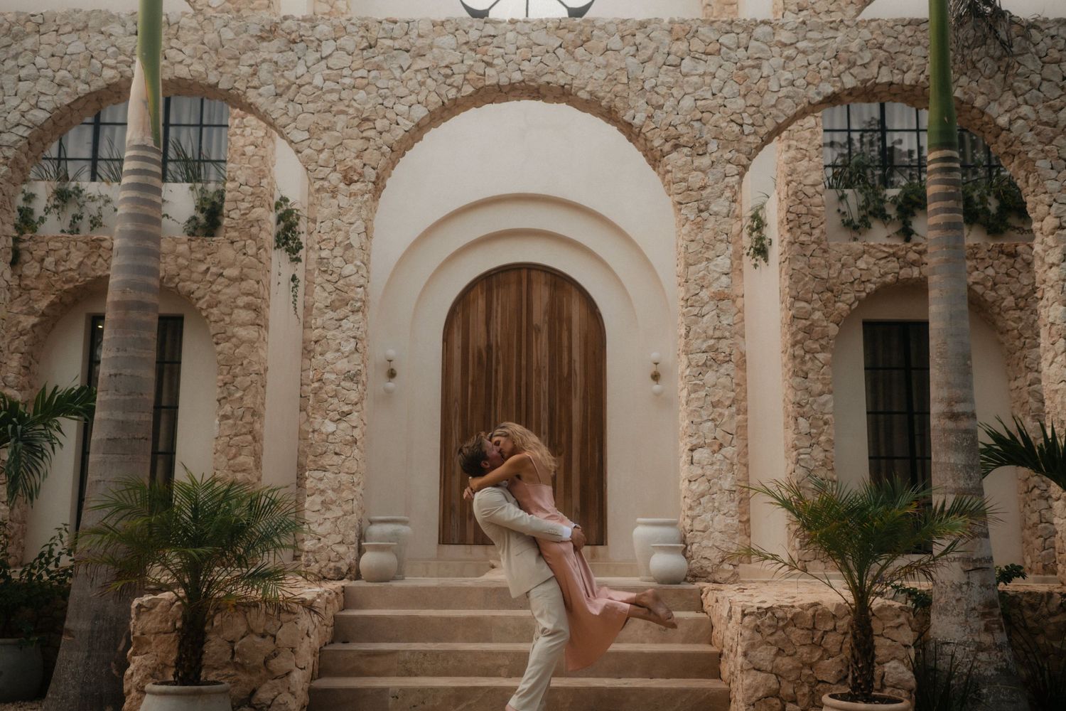 Romantic couple embracing outside Mediterranean style stone archway.