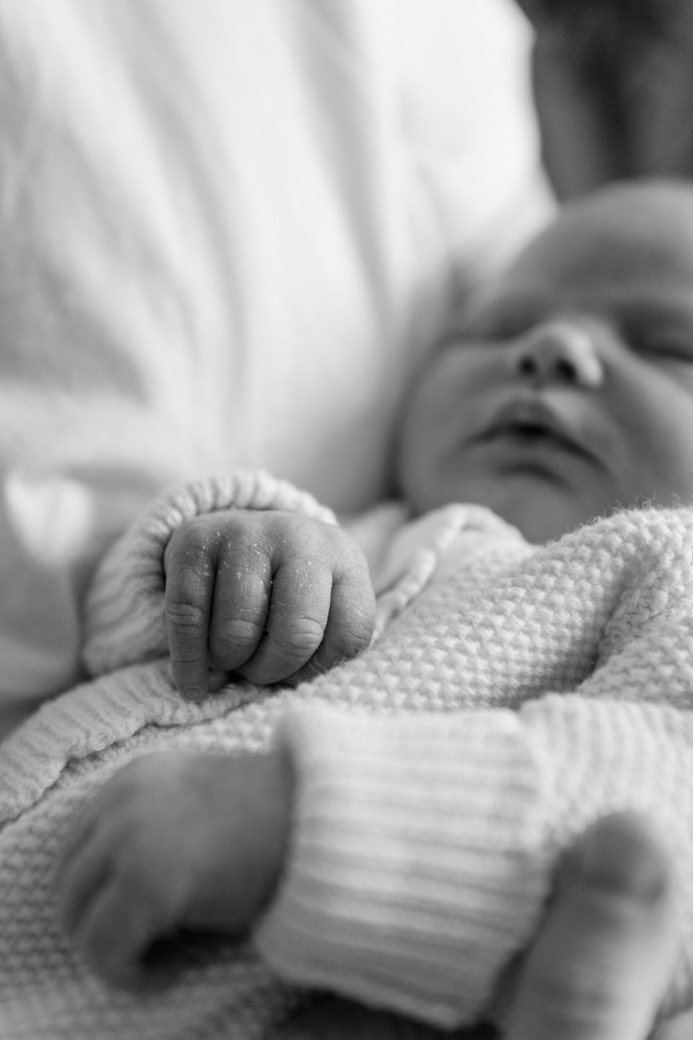 Close-up view of a baby's tiny hand grasping a soft white knitted blanket in black and white.