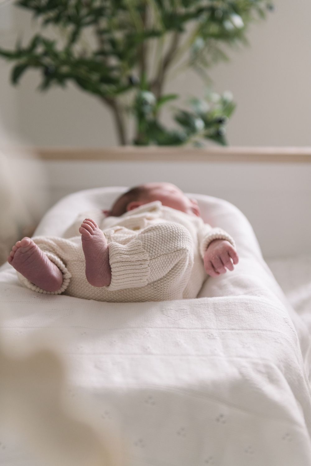 A baby's tiny feet wearing a white knit sweater while resting on soft white bedding.