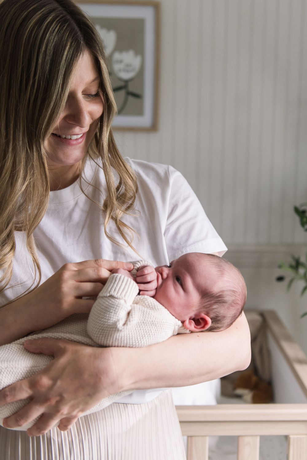 A mother in a white shirt tenderly holds and gazes at her newborn baby wrapped in a light pink blanket.