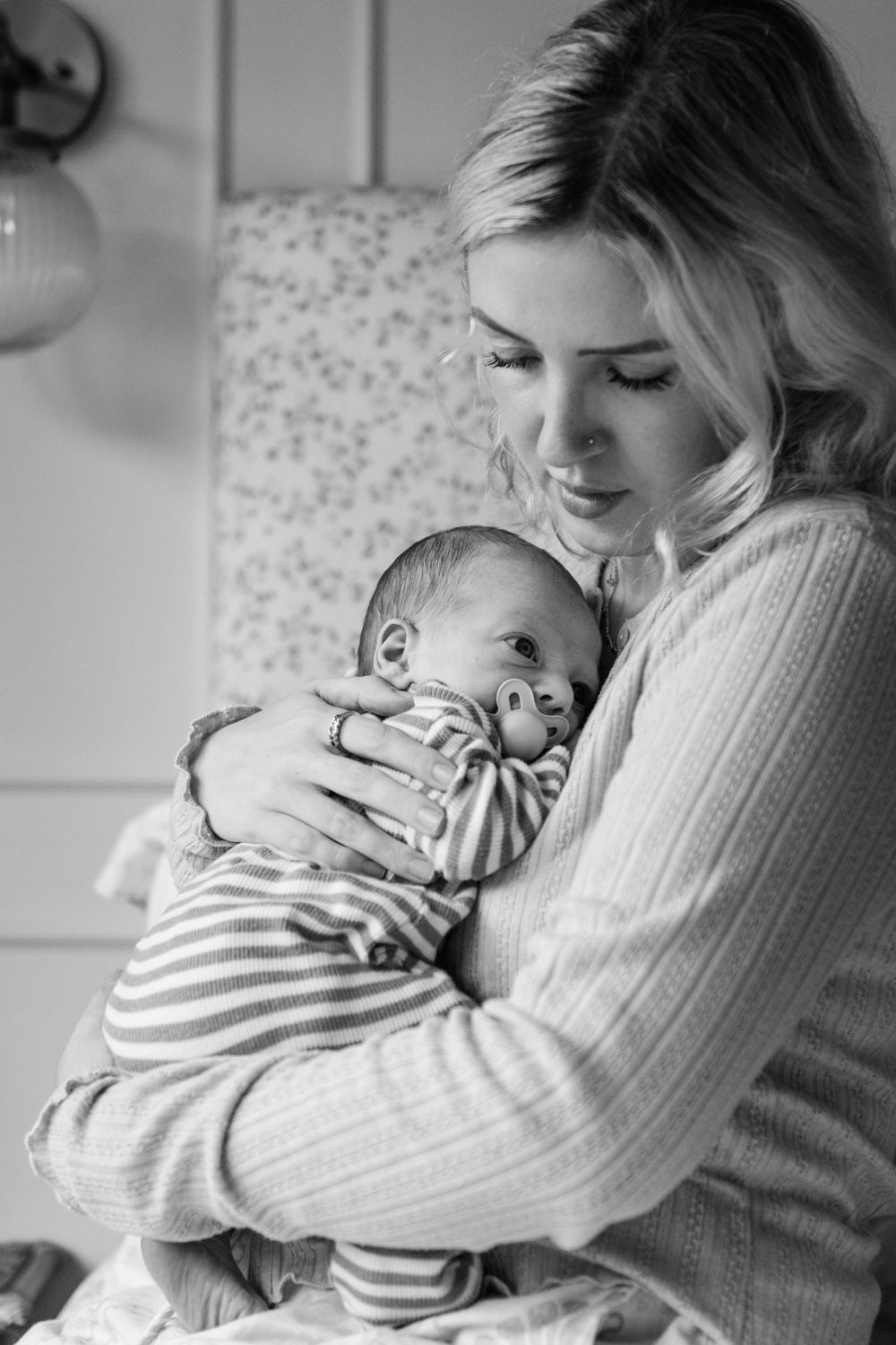 A tender moment captured in black and white as a parent in a cozy sweater cuddles their sleeping newborn in striped clothing.