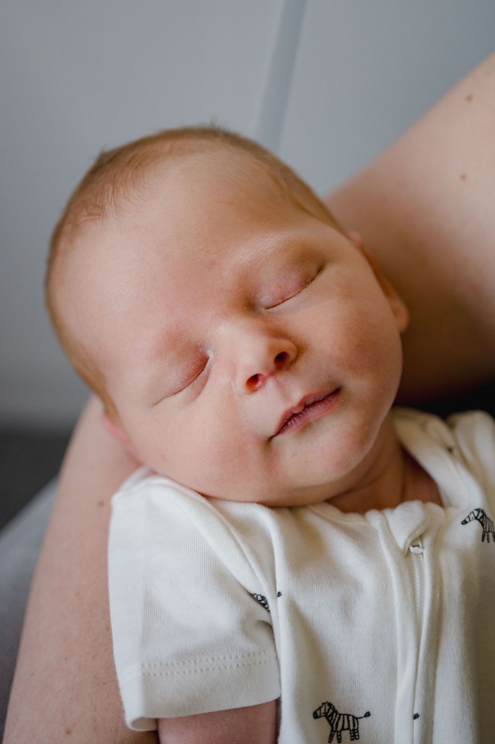 A sleeping baby in white clothing rests peacefully against a light background.