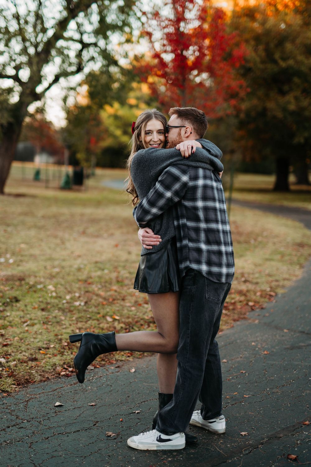 Couple sharing a romantic embrace on an autumn path surrounded by colorful fall foliage.