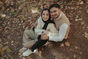 Couple in coordinated beige outfits sitting together on autumn ground.