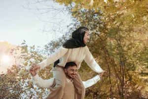 Joyful couple playing and laughing together in golden autumn forest.