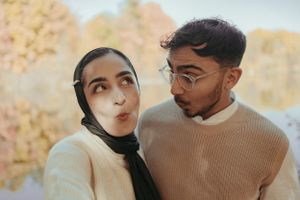 Couple in warm autumn tones making playful expressions while wearing coordinated beige and tan outfits outdoors.