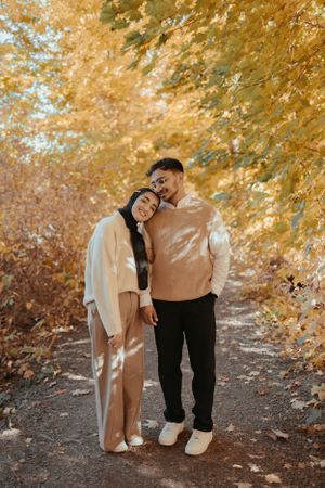 Couple in matching neutral tones embracing on path surrounded by golden autumn foliage.
