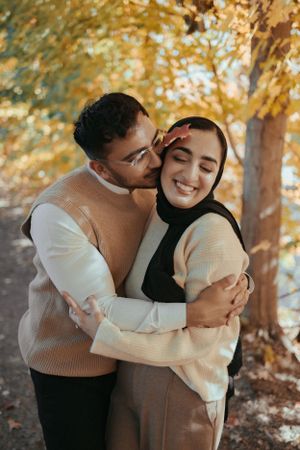Intimate moment captured between couple in neutral sweaters amid golden autumn trees.