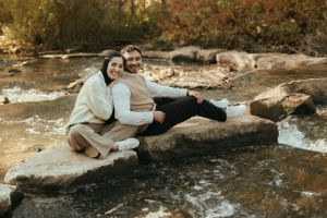 Couple relaxing together on large rocks by stream during autumn photoshoot.