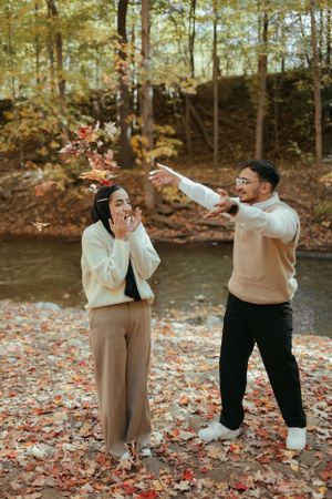 Playful autumn moment as couple throws fallen leaves in the air by waterside.