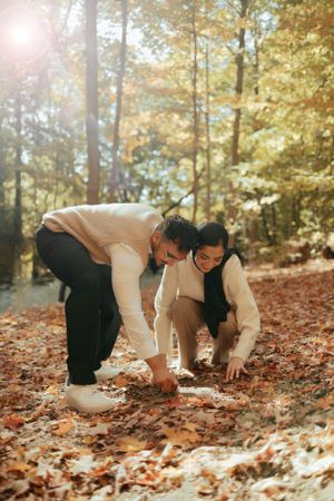 Couple in coordinated outfits bending down to gather fallen autumn leaves.