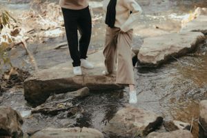Two people carefully walking across wet rocks near a stream.