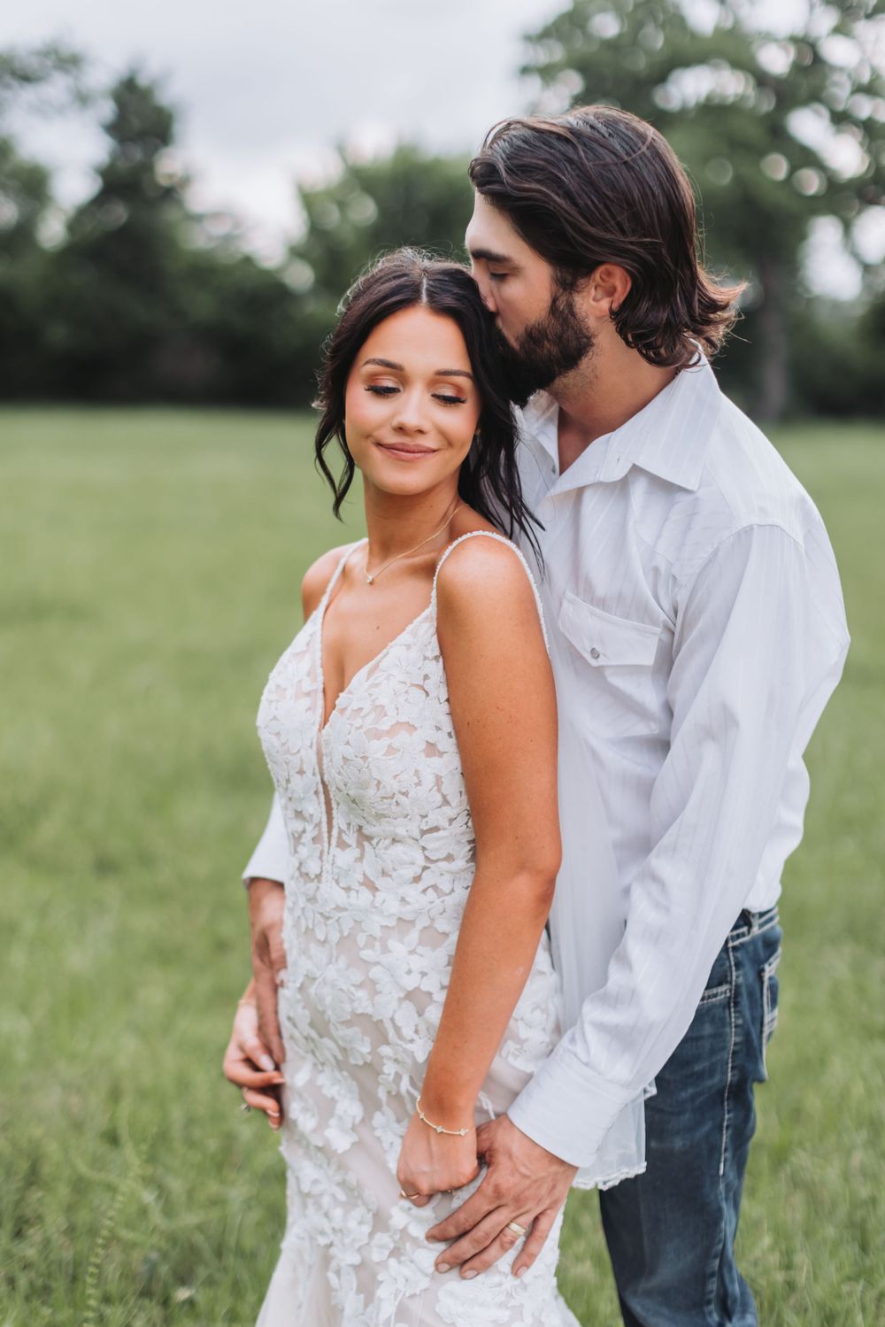 Couple shares intimate moment in field with bride wearing lace wedding dress.